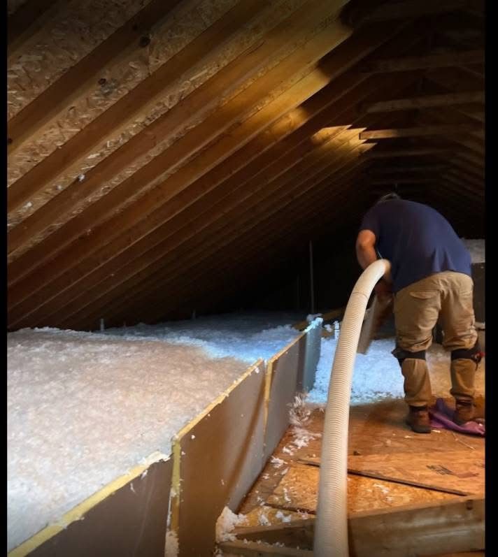 Technician blowing loose-fill insulation across an attic floor, viewed from above