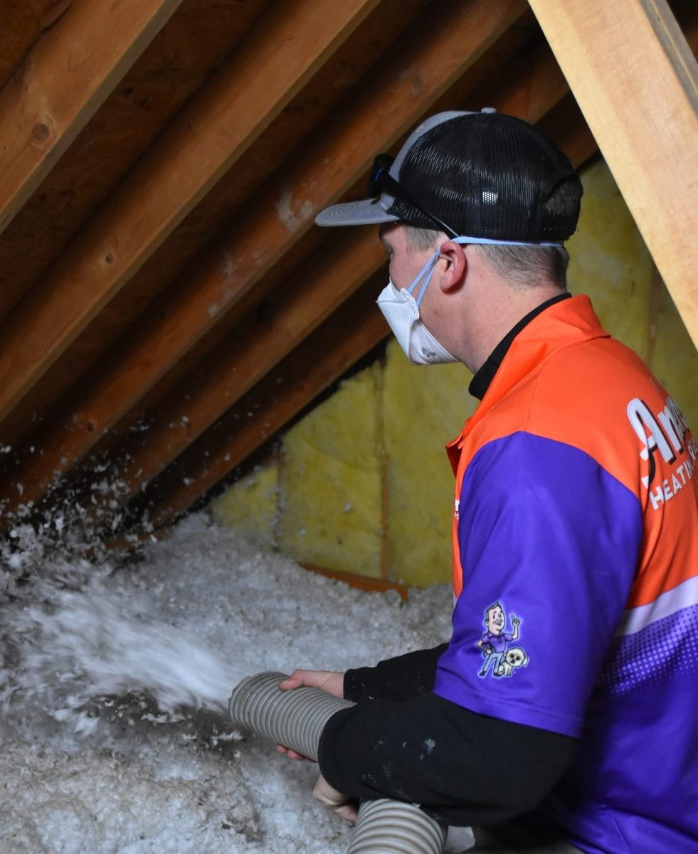 Anderson technician in branded uniform and respirator blowing loose-fill attic insulation