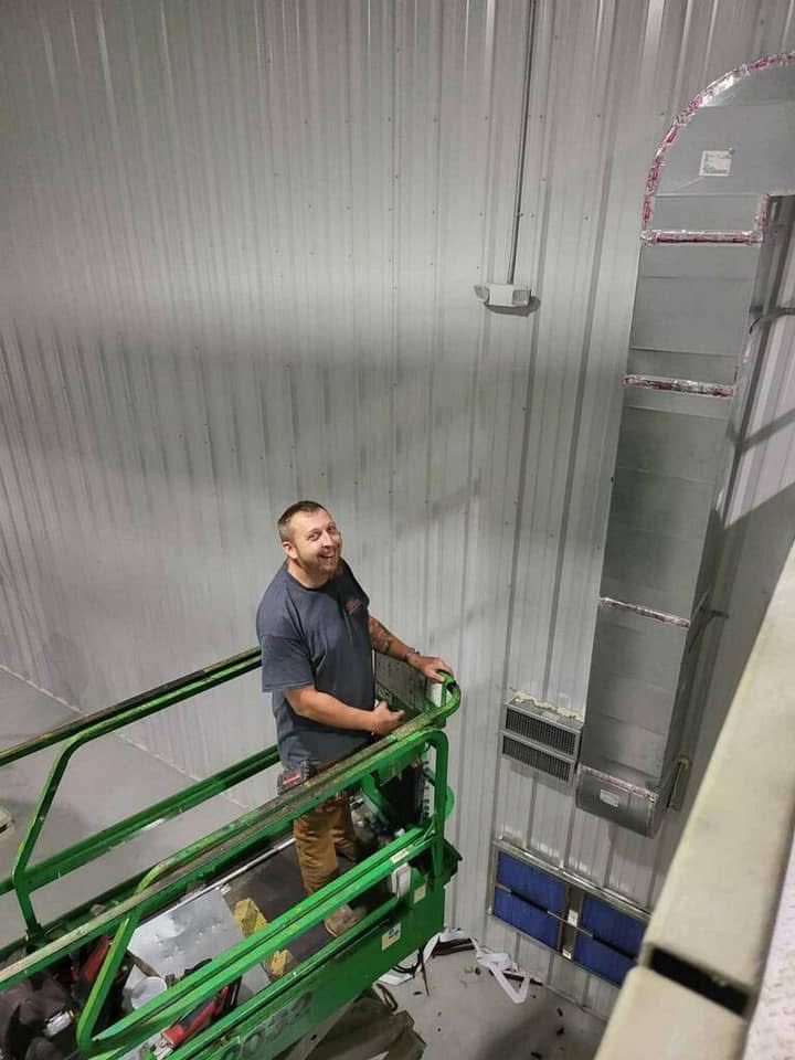 Anderson technician beside a tall custom commercial air handler and ductwork inside a metal building