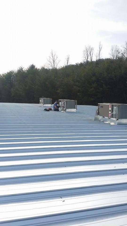Commercial rooftop HVAC units on a large metal roof with a technician servicing them