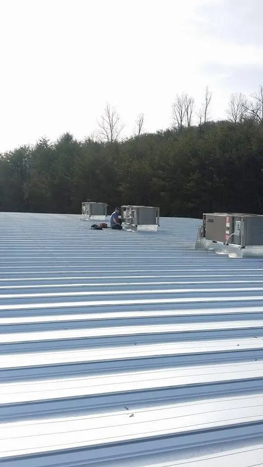 Commercial rooftop HVAC units on a large metal roof with a technician servicing them