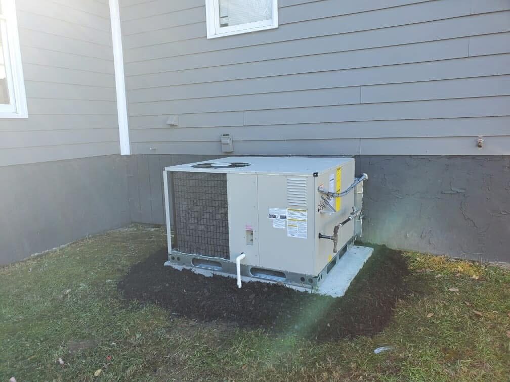 New gas package HVAC unit set on a concrete pad with fresh mulch beside a home