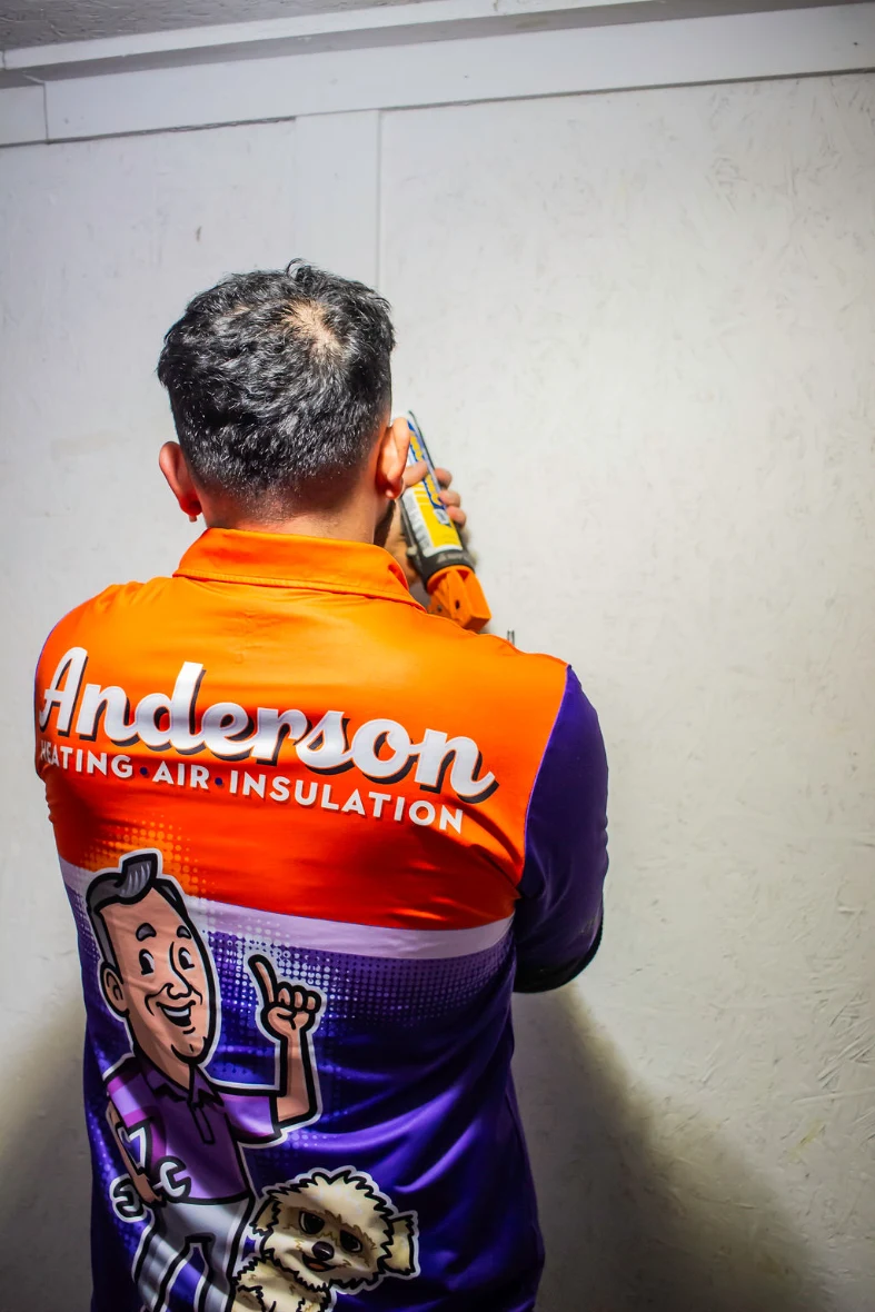 Anderson technician sealing air leaks along a wall with a sealant gun