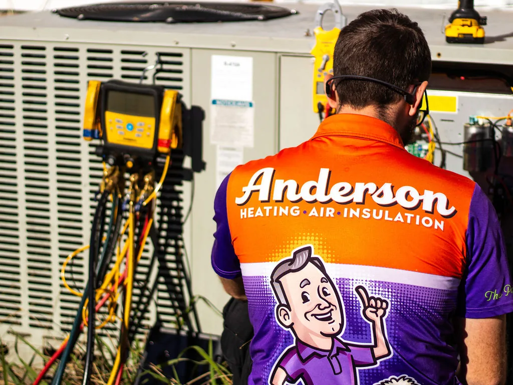 Anderson technician diagnosing an outdoor AC condenser with refrigerant gauges on a service call