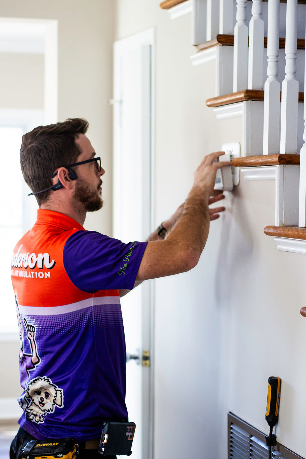 Anderson Heating, Air & Insulation technician servicing a residential thermostat as part of routine HVAC maintenance — the kind of preventive check covered by The Paws-itive Maintenance Plan.