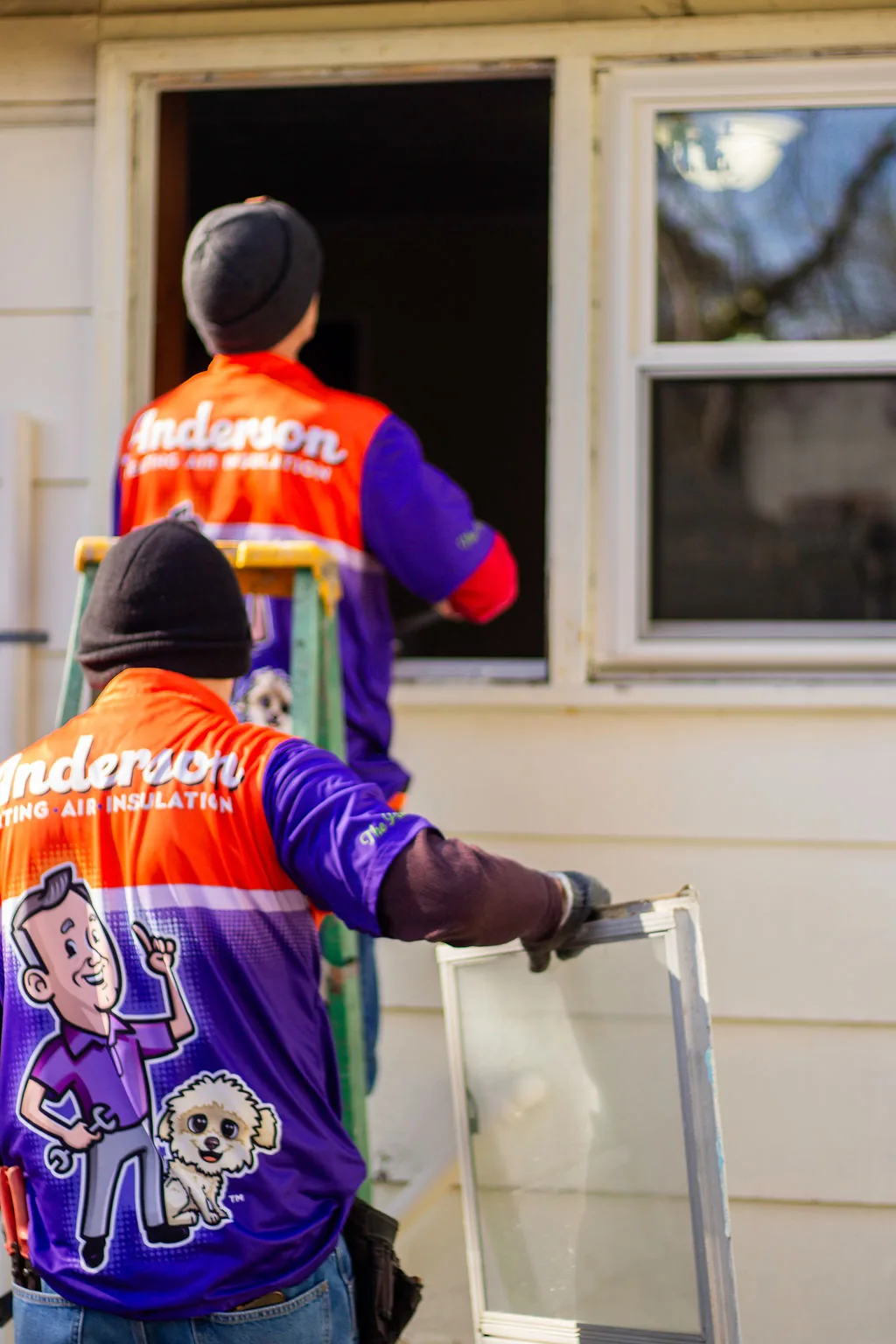 Two Anderson crew members removing an old window sash during a window replacement
