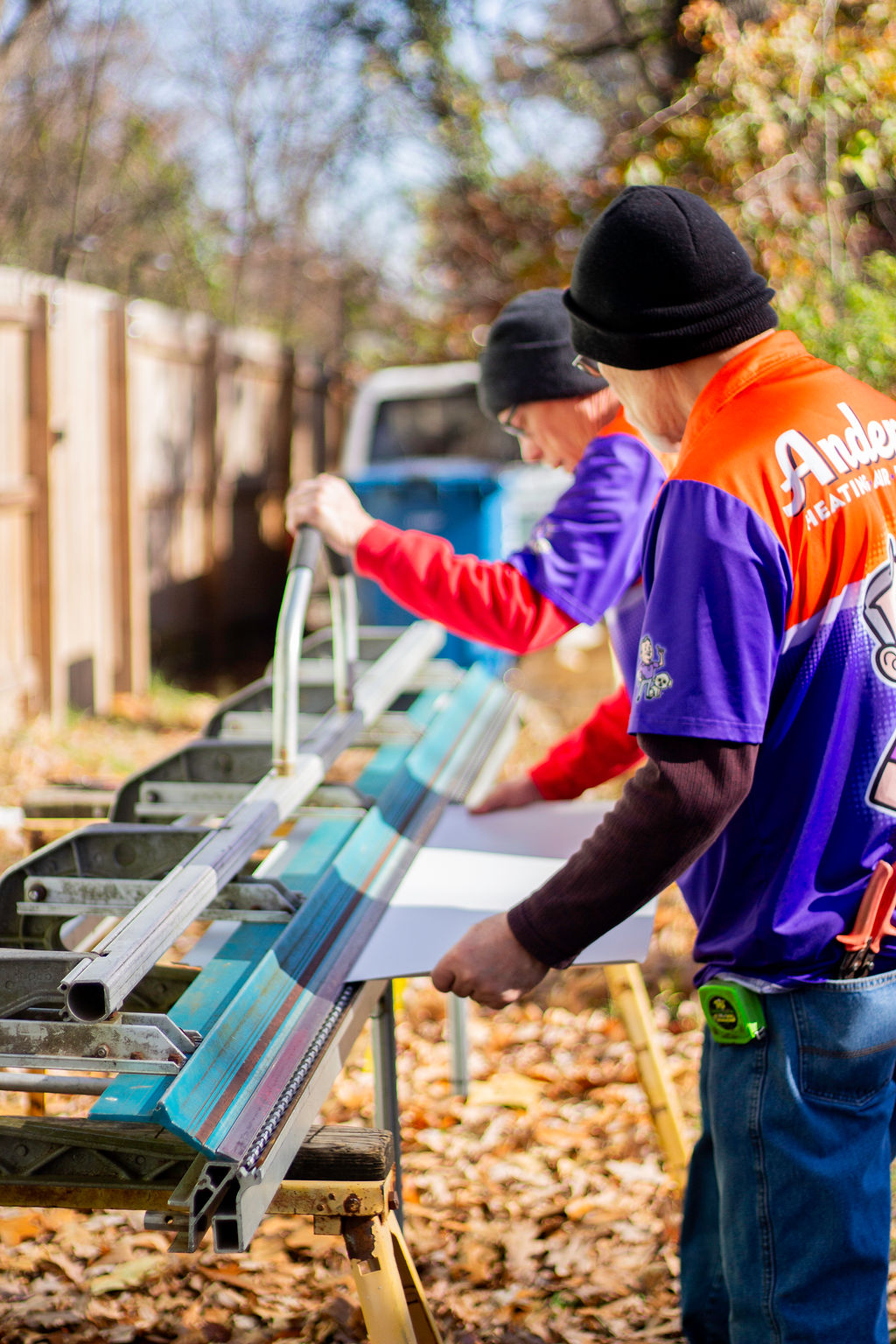 Two Anderson Heating, Air & Insulation team members measuring and cutting sheet metal at an outdoor workbench — the in-house sheet-metal shop serves Fairmount and Gordon County, GA.