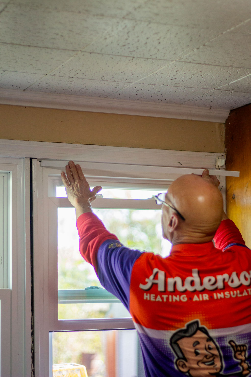 Anderson Heating, Air & Insulation technician installing white interior trim above a residential window — the finish work that determines whether the window install looks great or looks rushed.