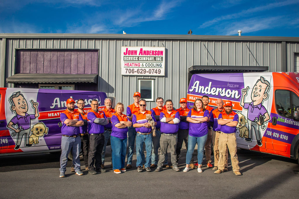 The Anderson Heating, Air & Insulation team standing in front of their 519 Pine Street Calhoun headquarters — the original John Anderson Service Company, Inc. sign visible behind them, flanked by branded service vans that cover Calhoun, Dalton, Rome, Cartersville and all of Northwest Georgia.