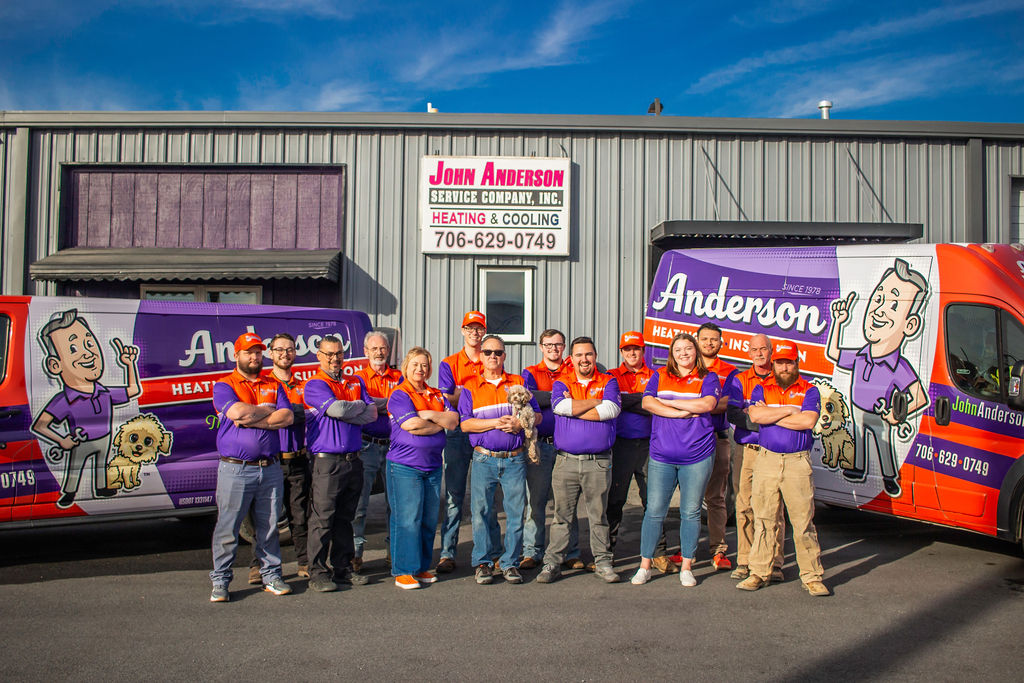 Anderson Heating, Air & Insulation team in front of the company's Calhoun, GA headquarters — the original John Anderson Service Company building, flanked by branded service vans serving Calhoun and Gordon County.