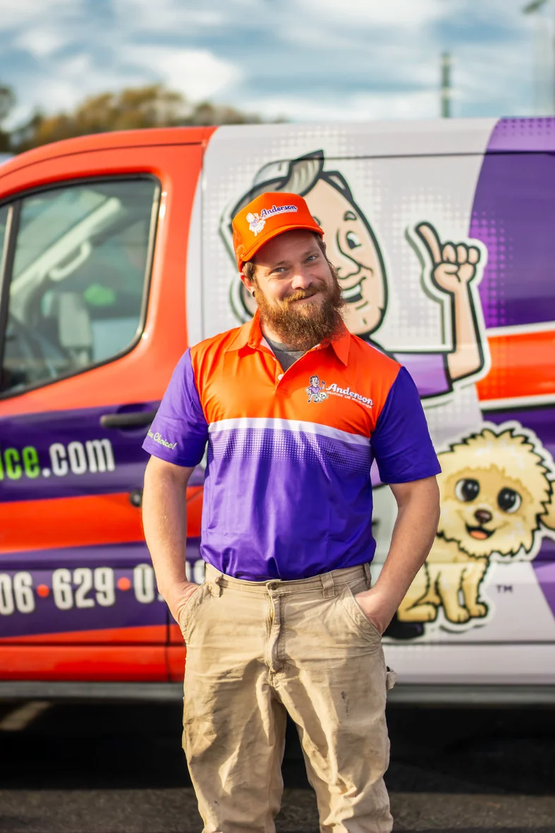 Smiling Anderson technician in a company uniform beside a branded Anderson service van