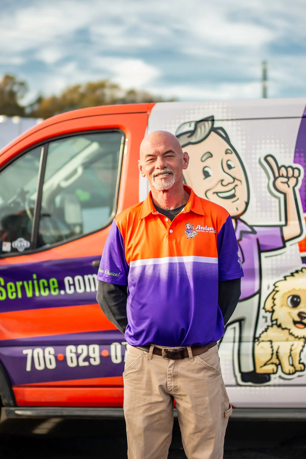 Veteran Anderson technician with a grey goatee smiling in front of a service van