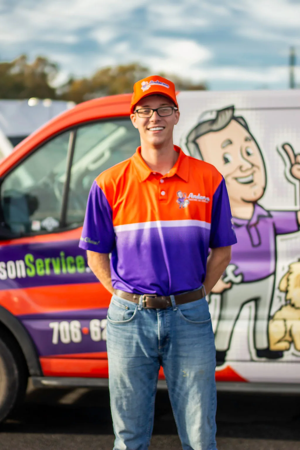 Young Anderson technician in glasses and an orange Anderson cap in front of a service van