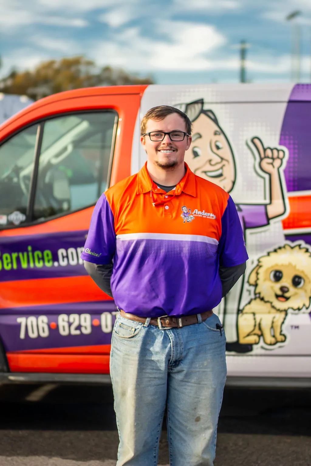 Smiling young Anderson technician with glasses in front of a service van