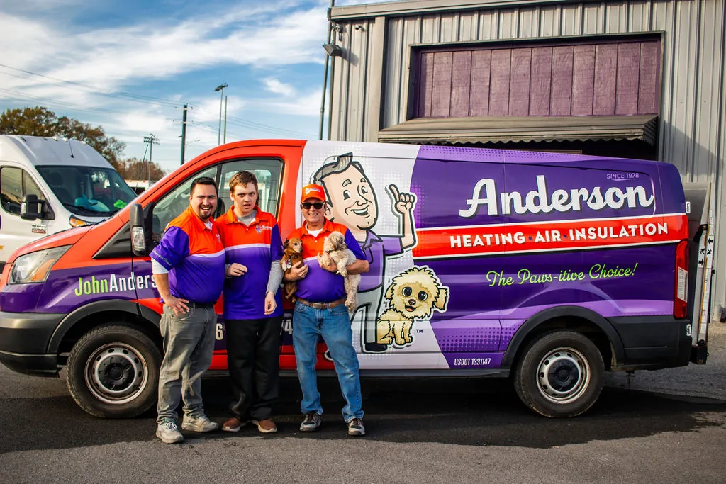 Three Anderson team members, one holding Gypsy, standing beside a fully wrapped Anderson service van