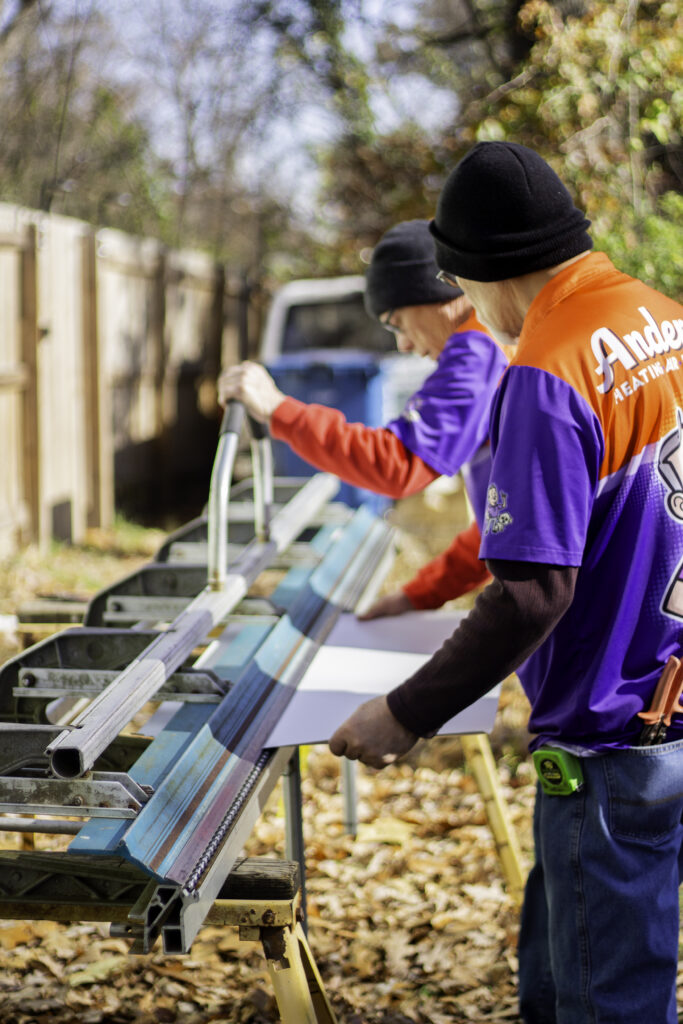 Anderson Heating technicians using a metal brake to fabricate custom sheet metal ductwork for a commercial HVAC installation.